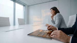 Une femme et un homme utilisent une tablette numérique avec une interface holographique lors d'une réunion professionnelle.